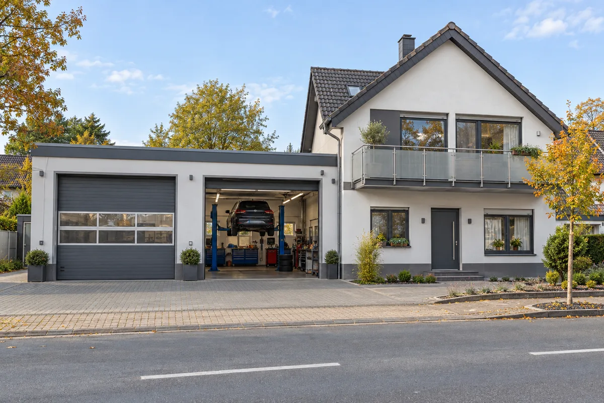 Kfz-Werkstatt mit zwei großen Sektionaltoren und Firmenschild im Erdgeschoss, darüber eine Wohnung mit Fenstern und Balkon