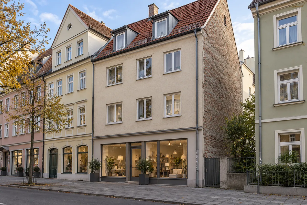Schlichtes Wiederaufbauhaus der Nachkriegszeit auf schmaler alter Parzelle mit Putzfassade, ziegelsichtiger Seitenwand und kleinem Laden in Augsburg